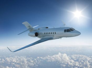 Private jet flies past sun - in blue sky above the clouds